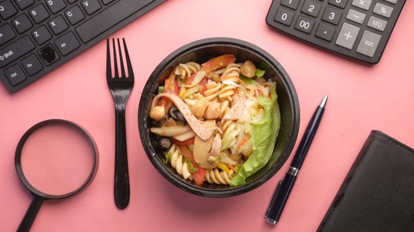 a bowl of pasta salad next to a keyboard and a pair of scissors